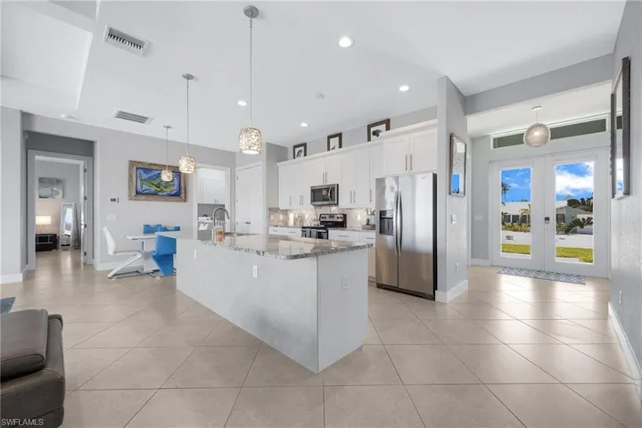 Kitchen with appliances with stainless steel finishes, light stone counters, white cabinets, recessed lighting, and a center island with sink