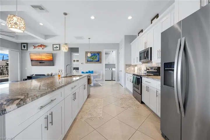 Kitchen featuring appliances with stainless steel finishes, white cabinets, light stone counters, hanging light fixtures, and recessed lighting