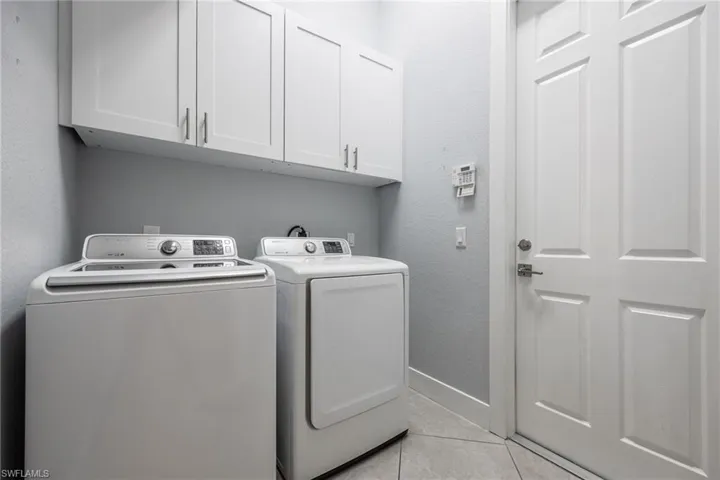 Laundry room with a textured wall, cabinet space, washer and clothes dryer, and light tile patterned flooring