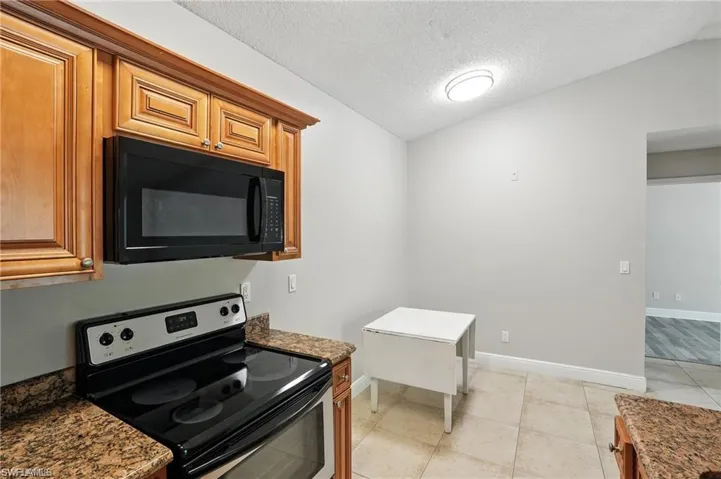 Kitchen with stainless steel electric range oven, black microwave, dark stone countertops, light tile patterned floors, and a textured ceiling