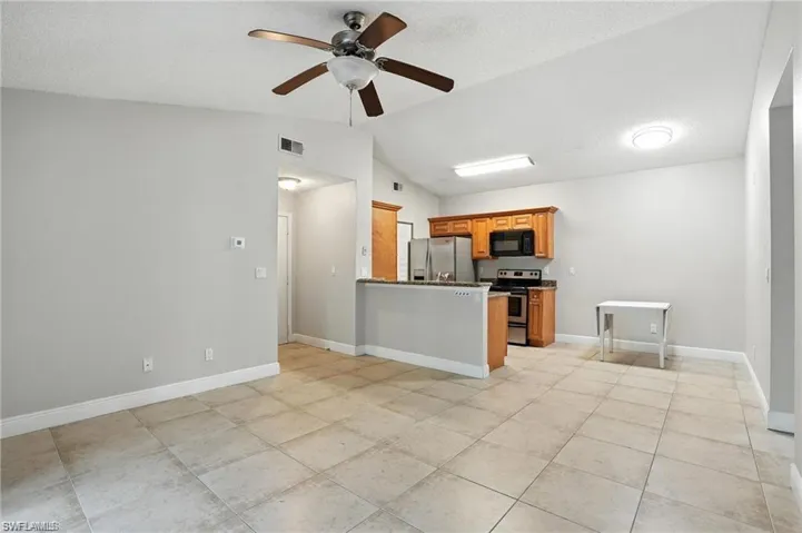 Kitchen featuring stainless steel appliances, lofted ceiling, brown cabinetry, ceiling fan, and a peninsula