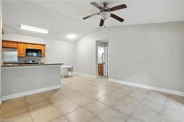 Kitchen featuring black microwave, stainless steel fridge, a ceiling fan, lofted ceiling, and range with electric stovetop