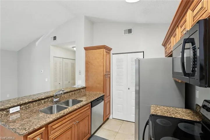 Kitchen with stainless steel dishwasher, electric stove, black microwave, vaulted ceiling, and a peninsula