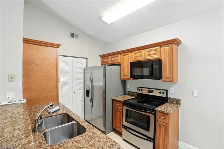 Kitchen with stainless steel appliances, lofted ceiling, stone counters, brown cabinetry, and a textured ceiling