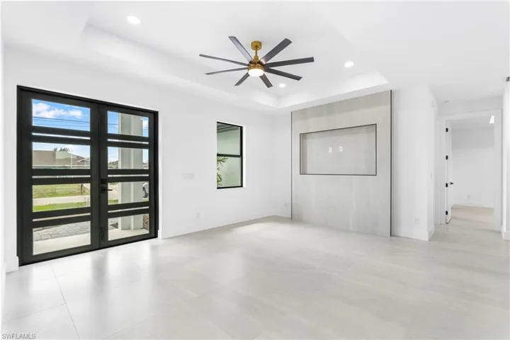 Expansive living area featuring large format light-toned tile flooring, a tray ceiling with recessed lighting, and a modern ceiling fan