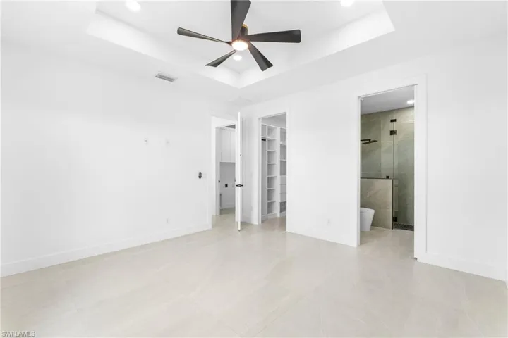 Spacious bedroom featuring light-toned tile flooring, a tray ceiling with recessed lighting, and a modern ceiling fan