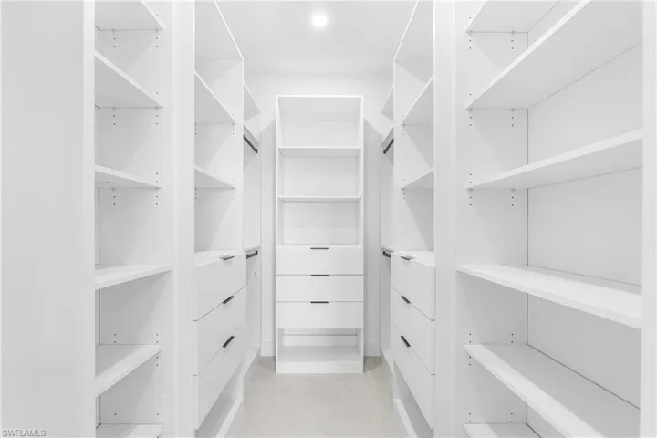 Custom-designed walk-in closet featuring floor-to-ceiling white shelving, integrated drawers with dark hardware, and ample hanging space