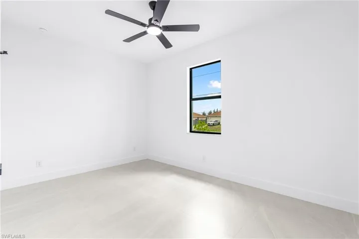 Bright interior room featuring a modern ceiling fan with integrated lighting, a single window with black framing, and light-toned flooring