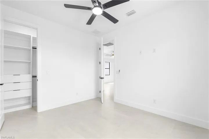 White-painted room featuring light-toned flooring, a ceiling fan with integrated lighting, and a built-in closet system with shelving and drawers
