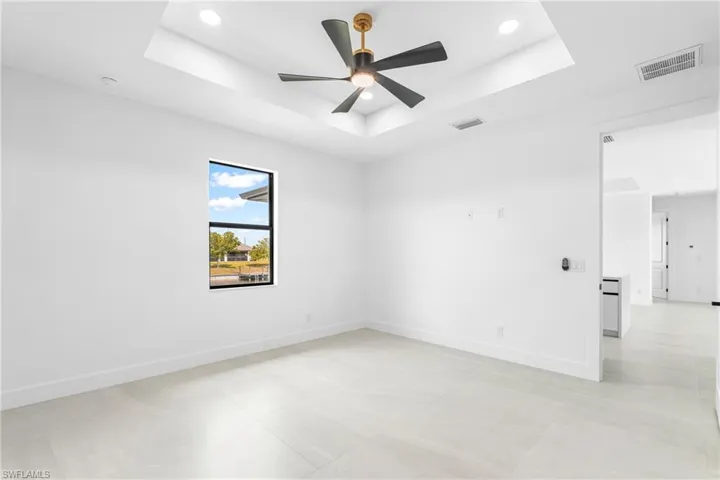Spacious room featuring light-toned tile flooring, a tray ceiling with recessed lighting, and a modern ceiling fan with black blades and a gold-finish accent