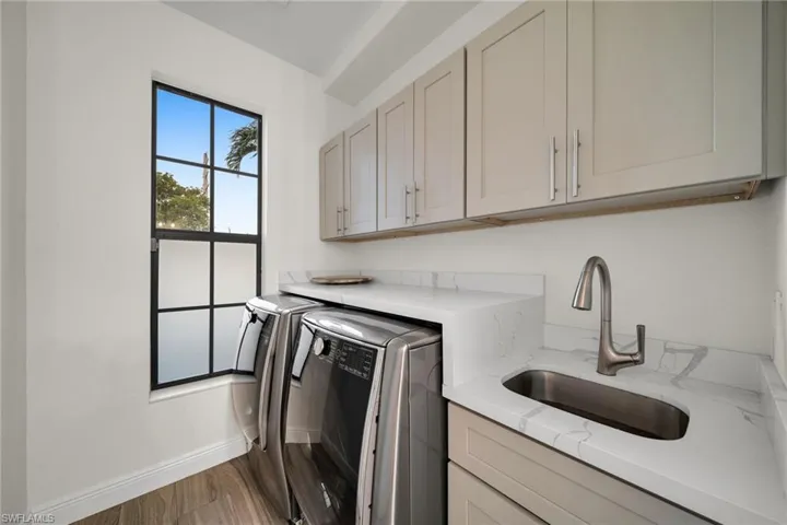 Laundry room with wood finished floors, a sink, cabinet space, washing machine and dryer, and baseboards
