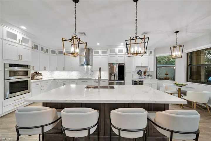 Kitchen featuring wall chimney range hood, stainless steel appliances, a chandelier, and a sink
