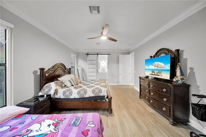 Bedroom with light wood-style flooring, a barn door, baseboards, visible vents, and crown molding