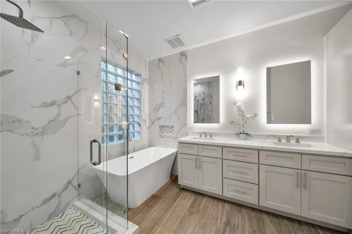 Full bath with a sink, a marble finish shower, double vanity, a freestanding bath, and visible vents