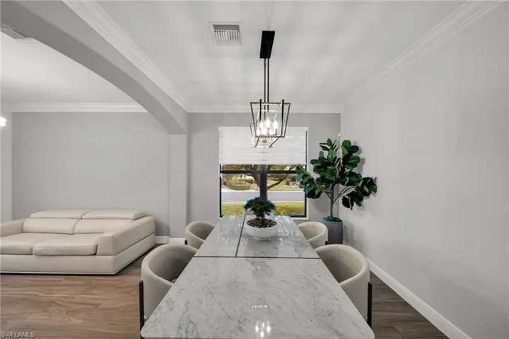 Dining space with crown molding, arched walkways, baseboards, a notable chandelier, and visible vents