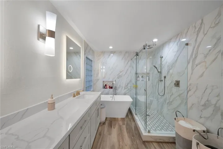 Bathroom with a marble finish shower, a freestanding bath, tile walls, wood finished floors, and vanity
