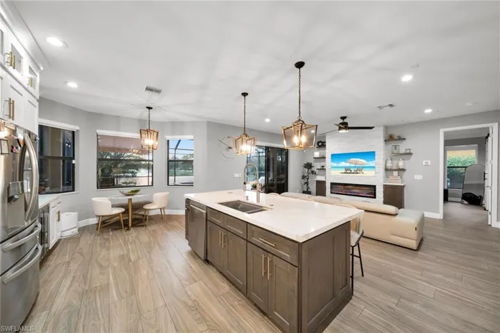 Kitchen featuring stainless steel appliances, a sink, visible vents, ceiling fan with notable chandelier, and a large fireplace