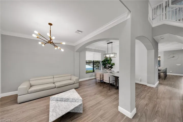 Living area with arched walkways, an inviting chandelier, baseboards, ornamental molding, and visible vents