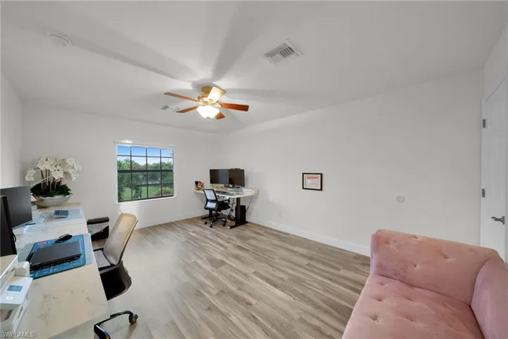 Home office featuring light wood finished floors, baseboards, a ceiling fan, and visible vents