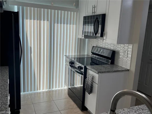 Kitchen featuring black appliances, dark stone counters, white cabinetry, backsplash, and light tile patterned floors