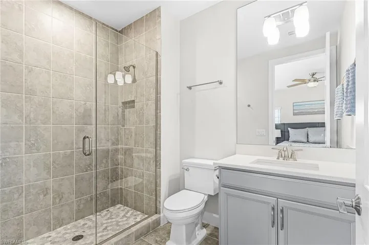 Glass-enclosed shower with gray square tile surround and pebble-finish flooring