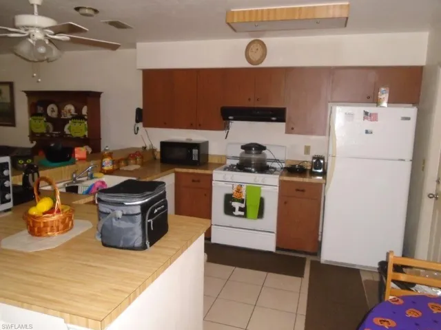 Kitchen featuring ceiling fan, white appliances, sink, exhaust hood, and light tile patterned floors