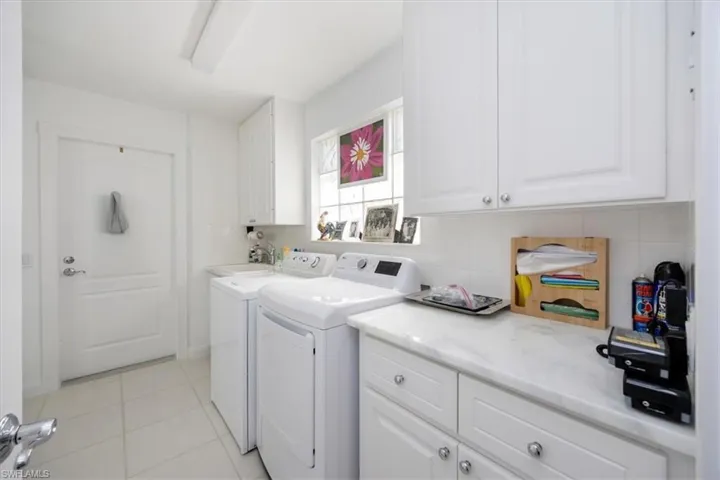 Laundry area with cabinets, washing machine and dryer, sink, and light tile patterned floors
