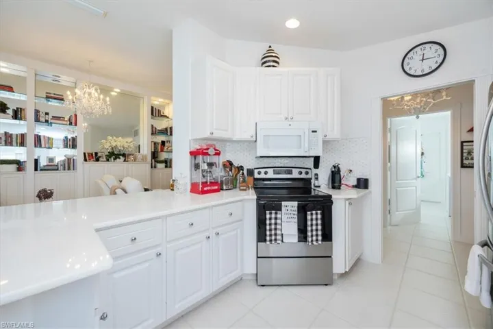 Kitchen with stainless steel range with electric stovetop, hanging light fixtures, backsplash, and white cabinets