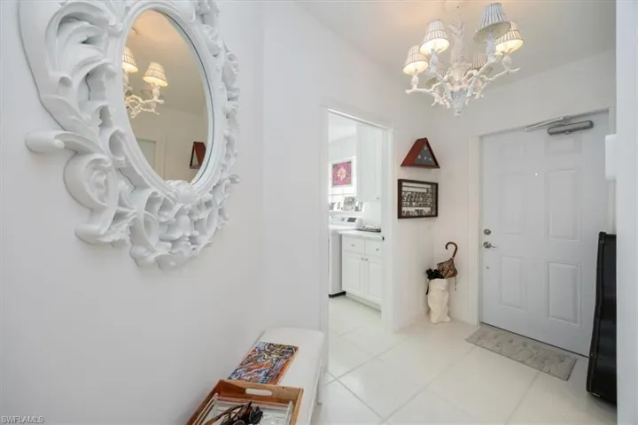 Foyer entrance with light tile patterned flooring, washer / dryer, and a notable chandelier