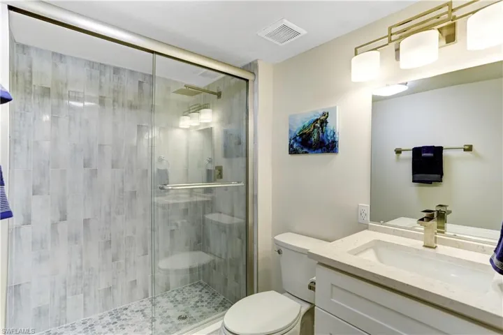 guest bathroom with glass shower doors, custom tile, quartz vanity
