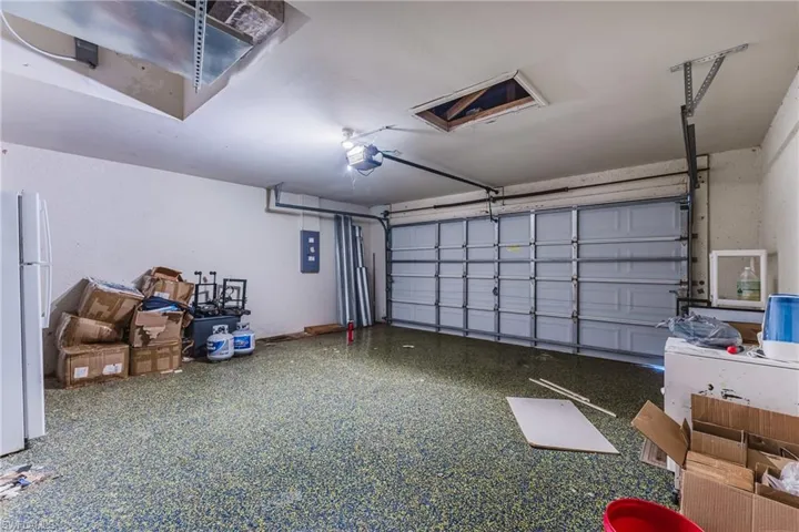 Garage with freestanding refrigerator, electric panel, and a garage door opener