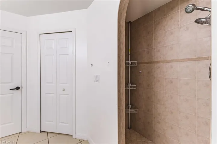 Bathroom featuring a closet, a tile shower, and light tile patterned floors