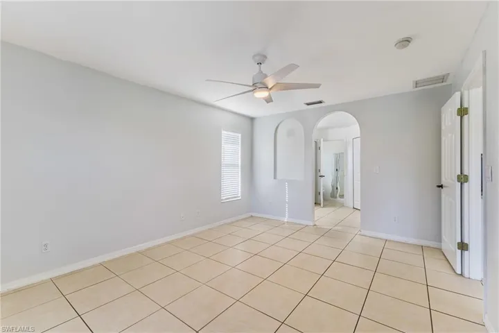 Unfurnished room with arched walkways, a ceiling fan, and light tile patterned floors