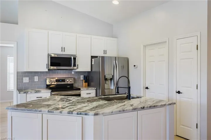 Kitchen featuring white cabinets, stainless steel appliances, light stone countertops, a kitchen island with sink, and recessed lighting