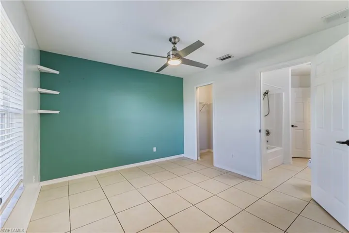 Unfurnished bedroom featuring a ceiling fan, ensuite bath, light tile patterned floors, and a walk in closet