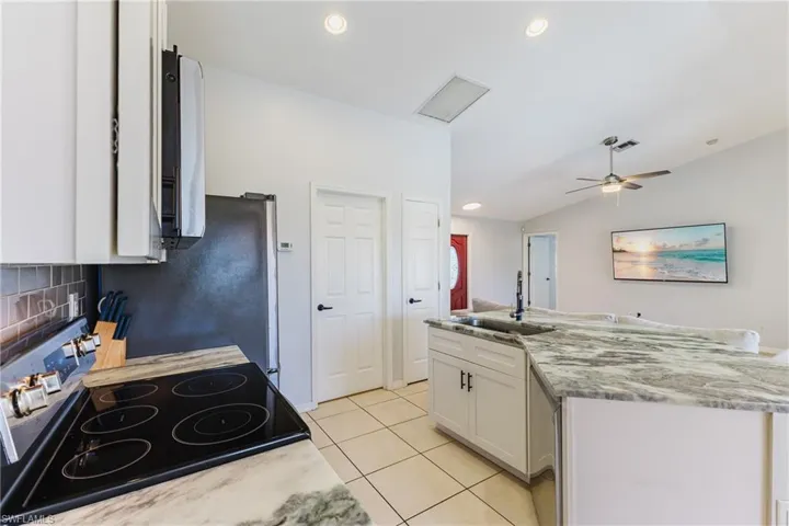 Kitchen featuring white cabinets, appliances with stainless steel finishes, recessed lighting, light tile patterned floors, and light stone counters