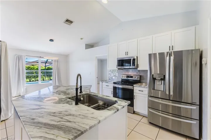 Kitchen with appliances with stainless steel finishes, white cabinetry, light tile patterned floors, light stone counters, and a kitchen island with sink