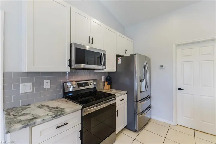 Kitchen featuring appliances with stainless steel finishes, white cabinetry, backsplash, light stone countertops, and light tile patterned floors