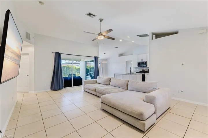 Living room with ceiling fan, high vaulted ceiling, light tile patterned floors, and recessed lighting