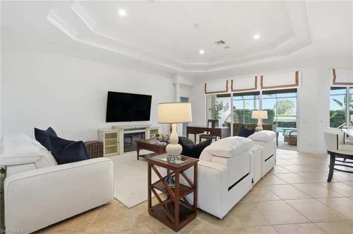 Living area with light tile patterned floors, a raised ceiling, recessed lighting, and ornamental molding