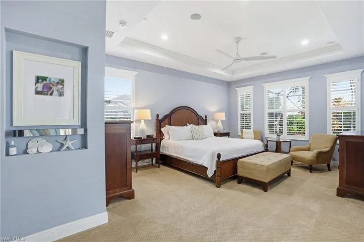 Bedroom with light colored carpet, a tray ceiling, multiple windows, ceiling fan, and recessed lighting