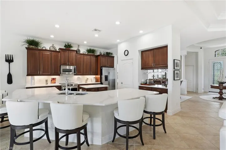Kitchen with tasteful backsplash, arched walkways, appliances with stainless steel finishes, a large island with sink, and a breakfast bar