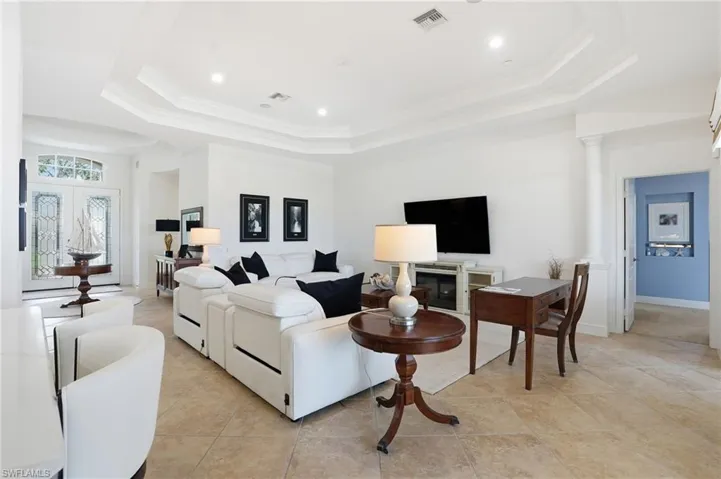Living area with ornamental molding, recessed lighting, light tile patterned floors, ornate columns, and a raised ceiling