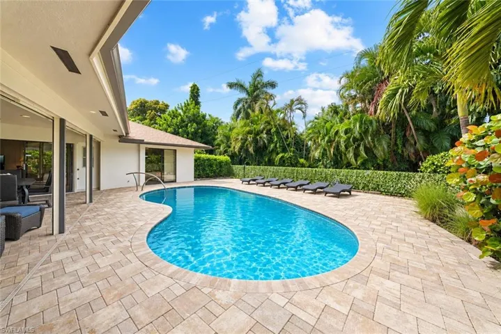 Curved pool with integrated handrail, surrounded by a paver patio and lush tropical landscaping