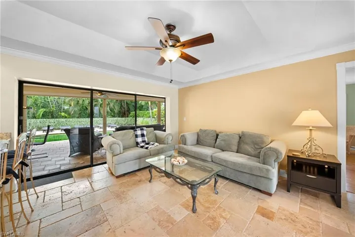 Tray ceiling with crown molding, ceiling fan, large format tile flooring, and sliding glass doors leading to an outdoor paved patio