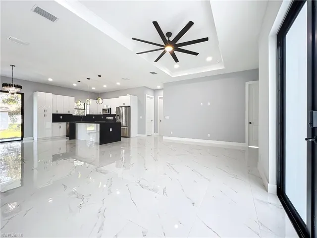 Kitchen featuring white cabinets, a raised ceiling, appliances with stainless steel finishes, pendant lighting, and a center island