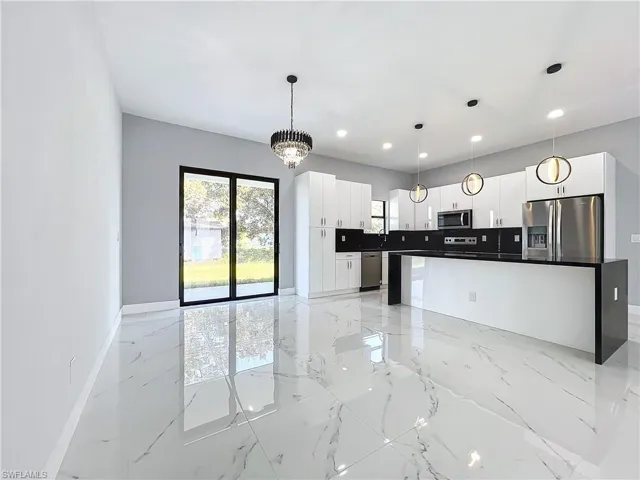 Kitchen featuring appliances with stainless steel finishes, a center island, hanging light fixtures, white cabinets, and an inviting chandelier