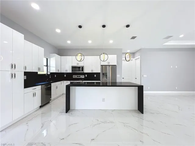Kitchen featuring decorative backsplash, stainless steel appliances, a center island, decorative light fixtures, and white cabinetry