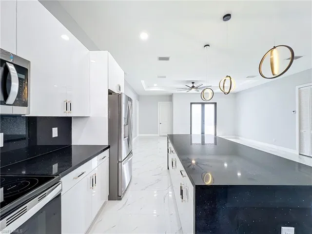 Kitchen featuring decorative backsplash, hanging light fixtures, stainless steel appliances, white cabinetry, and ceiling fan