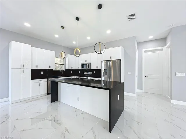 Kitchen with appliances with stainless steel finishes, white cabinetry, a center island, and pendant lighting